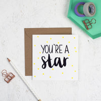 You're a star hand lettered square greeting card with black lettering and illustrated yellow stars