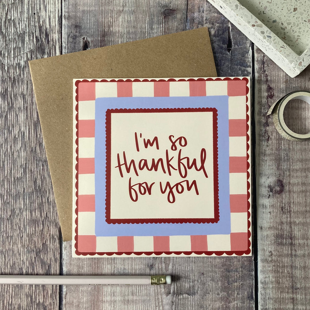 Greeting card with 'I'm so thankful for you' text on a checkered border, placed on a wooden surface.
