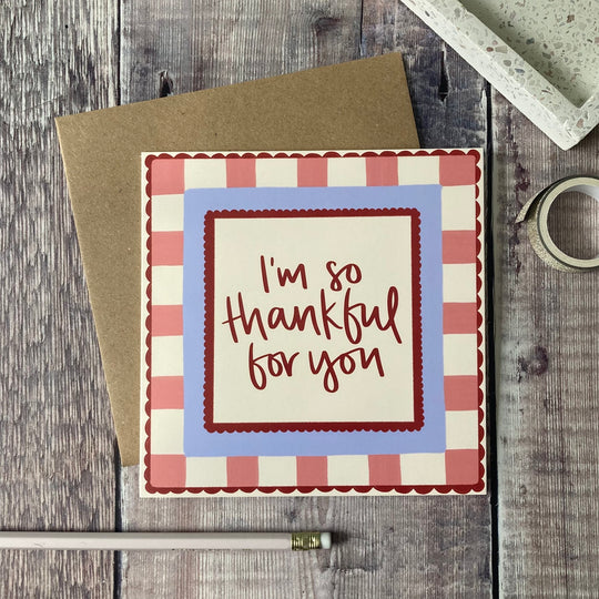 Greeting card with 'I'm so thankful for you' text on a checkered border, placed on a wooden surface.