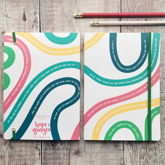 Two colorful notebooks with text on a wooden surface, featuring the brand 'Hope + Ginger'.