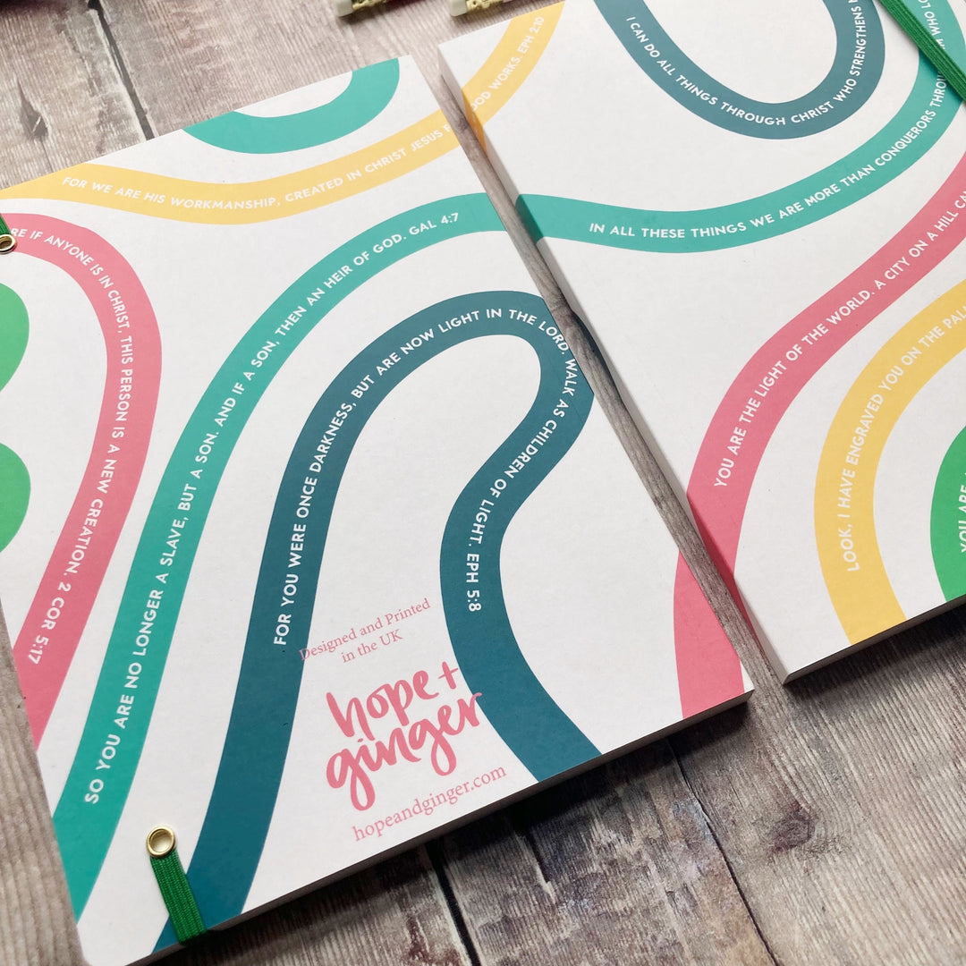 Two identity in Christ notebooks with colorful circular designs and text on a wooden surface