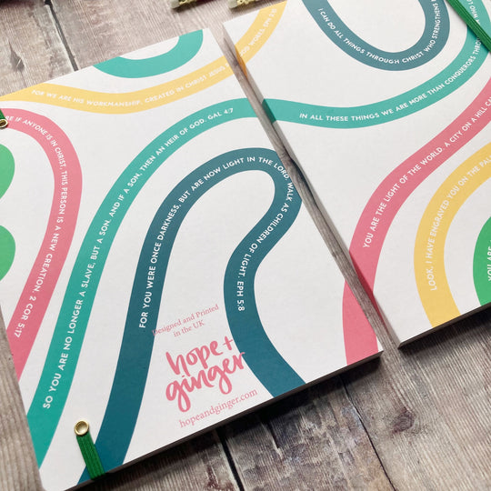 Two identity in Christ notebooks with colorful circular designs and text on a wooden surface