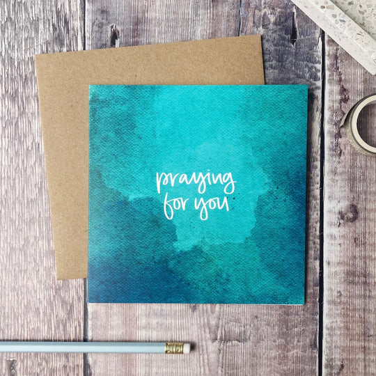 Card with 'Praying for you' text on a textured surface