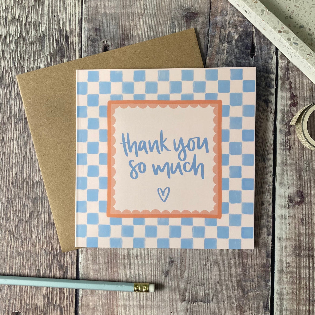 Card with 'thank you so much' text on a checkered background, placed on a wooden surface.