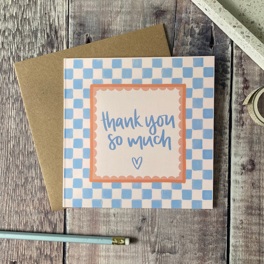 Card with 'thank you so much' text on a checkered background, placed on a wooden surface.