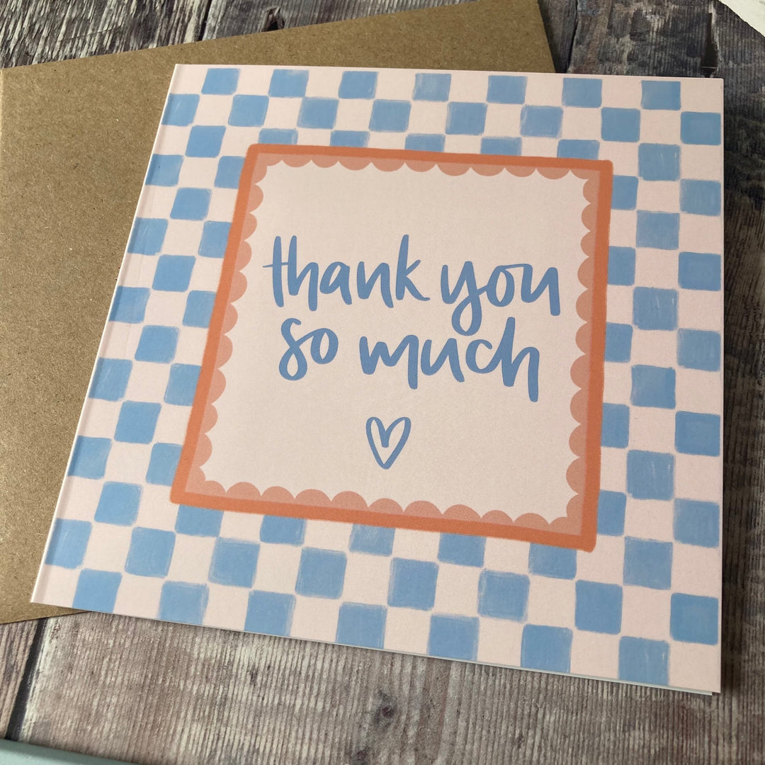 Card with 'thank you so much' text and checkered border on a wooden surface