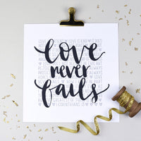 hand lettered print with Love never fails in black in the foreground and the words of 1 Corinthians 13 in the background