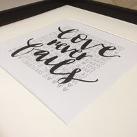 hand lettered print with Love never fails in black in the foreground and the words of 1 Corinthians 13 in the background